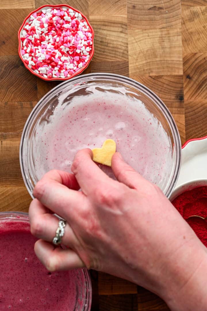 Dipping a mini heart cookie into light pink icing.