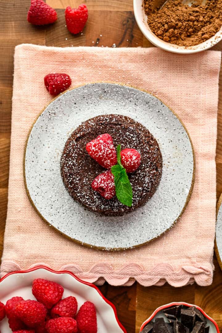 Baked chocolate lava cake on a small white plate topped with raspberries and mint.
