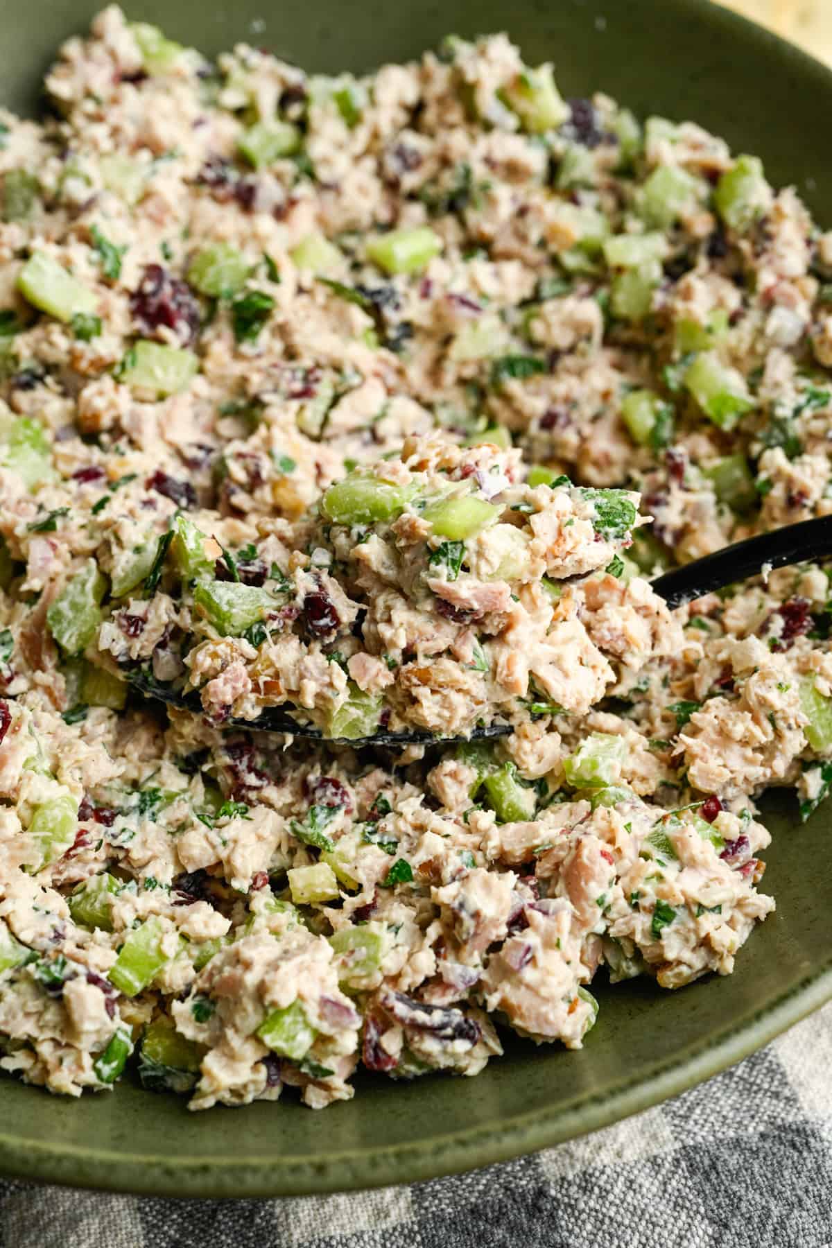 Close up view of cranberry walnut chicken salad in a green mixing bowl with a serving spoon in the bowl.