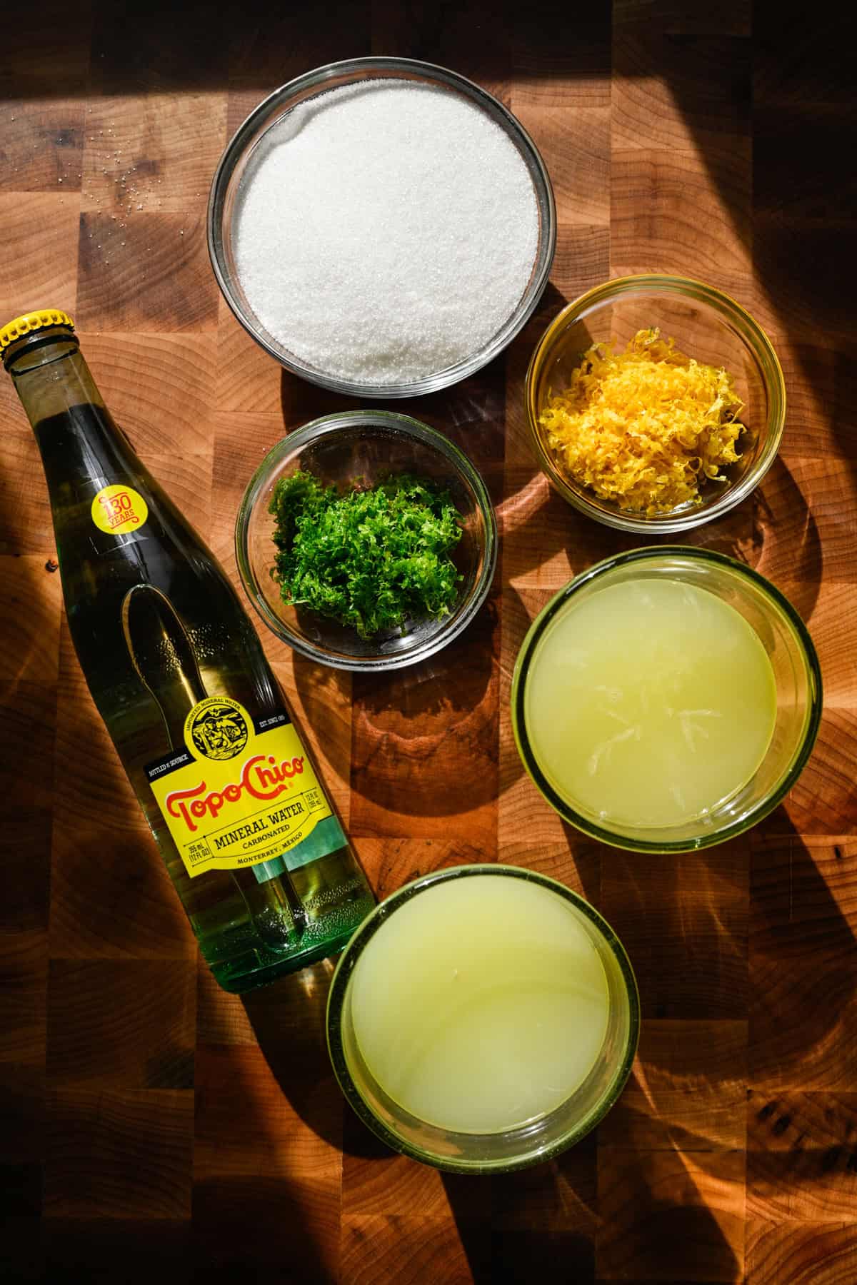 Overhead view of homemade sprite ingredients, including lemon and lime juice, zest, sugar, and sparkling water.