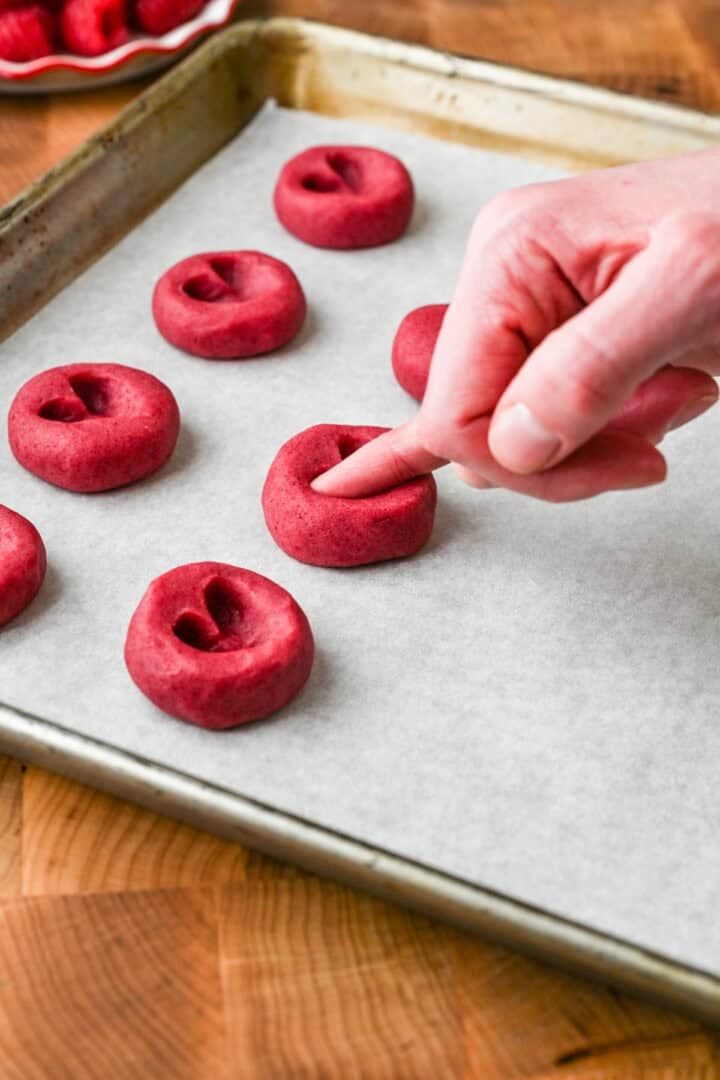 Using a pinky finger to create a heart-shaped indentation in the cookie.