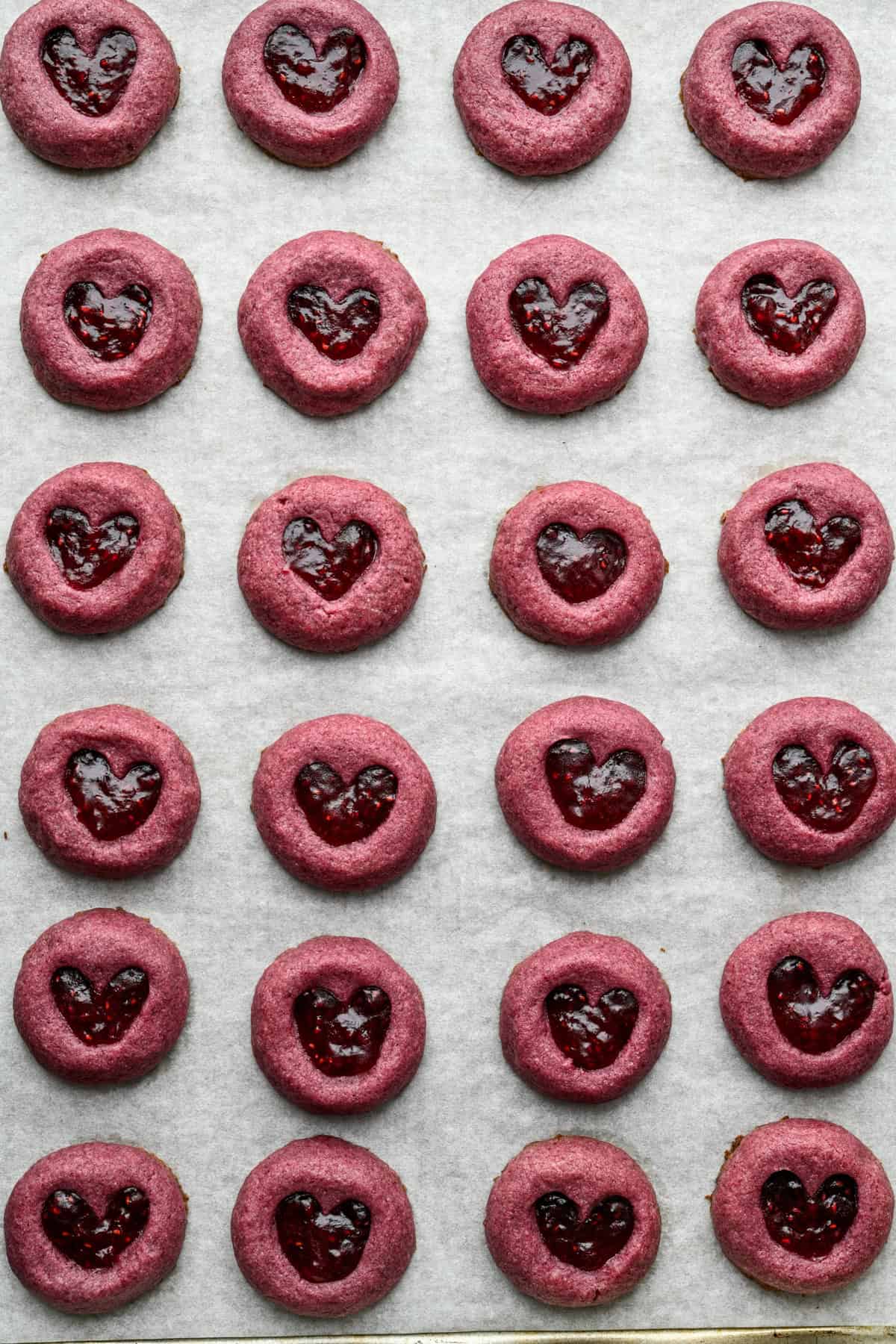 Raspberry heart thumbprint cookies on a sheet pan after baking.