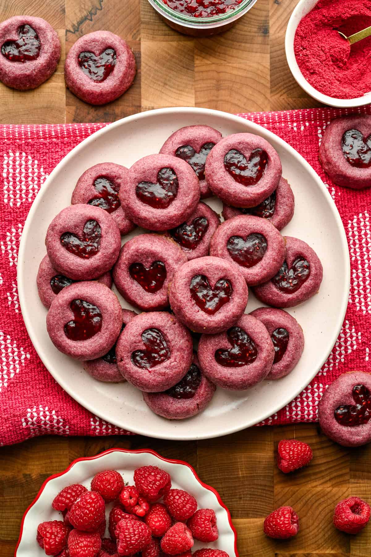 Raspberry heart thumbprint cookies piled up on a plate.