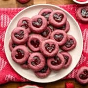 Raspberry heart thumbprint cookies piled up on a plate.