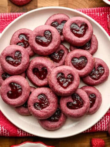 Raspberry heart thumbprint cookies piled up on a plate.