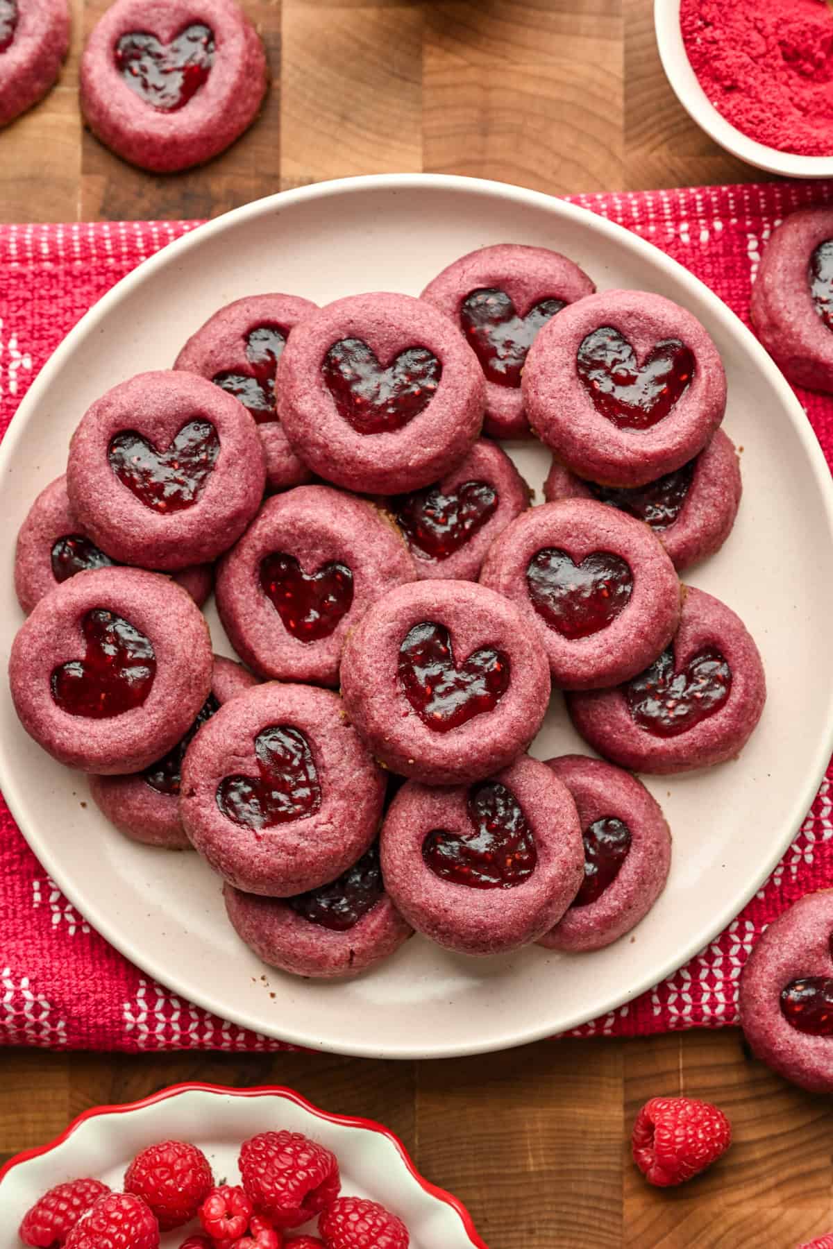 Raspberry heart thumbprint cookies piled up on a plate.