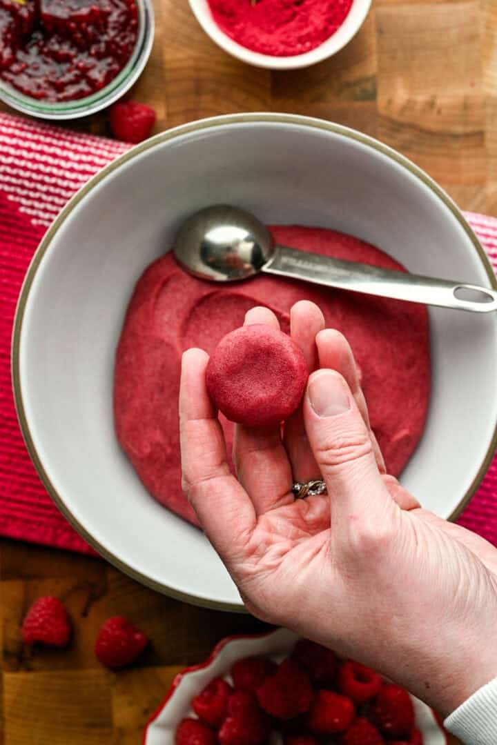 Hand holding a ball of Raspberry thumbprint cookie dough over a bowl.