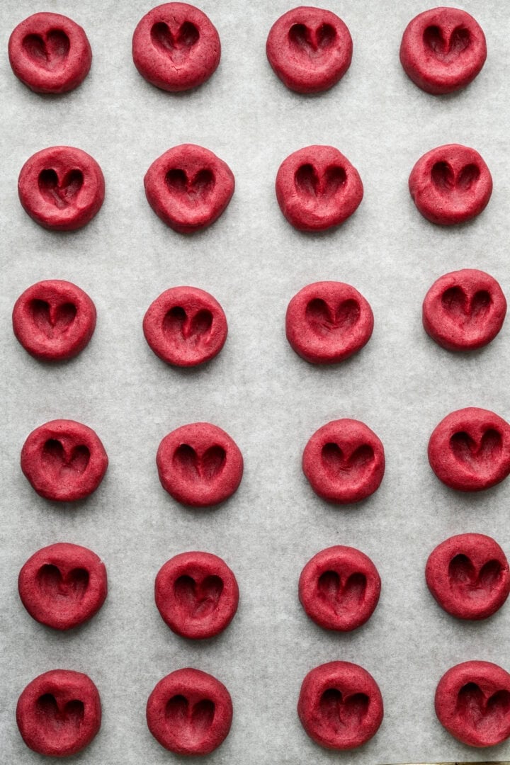 Raspberry heart thumbprint cookies on sheet pan before filling with jam.