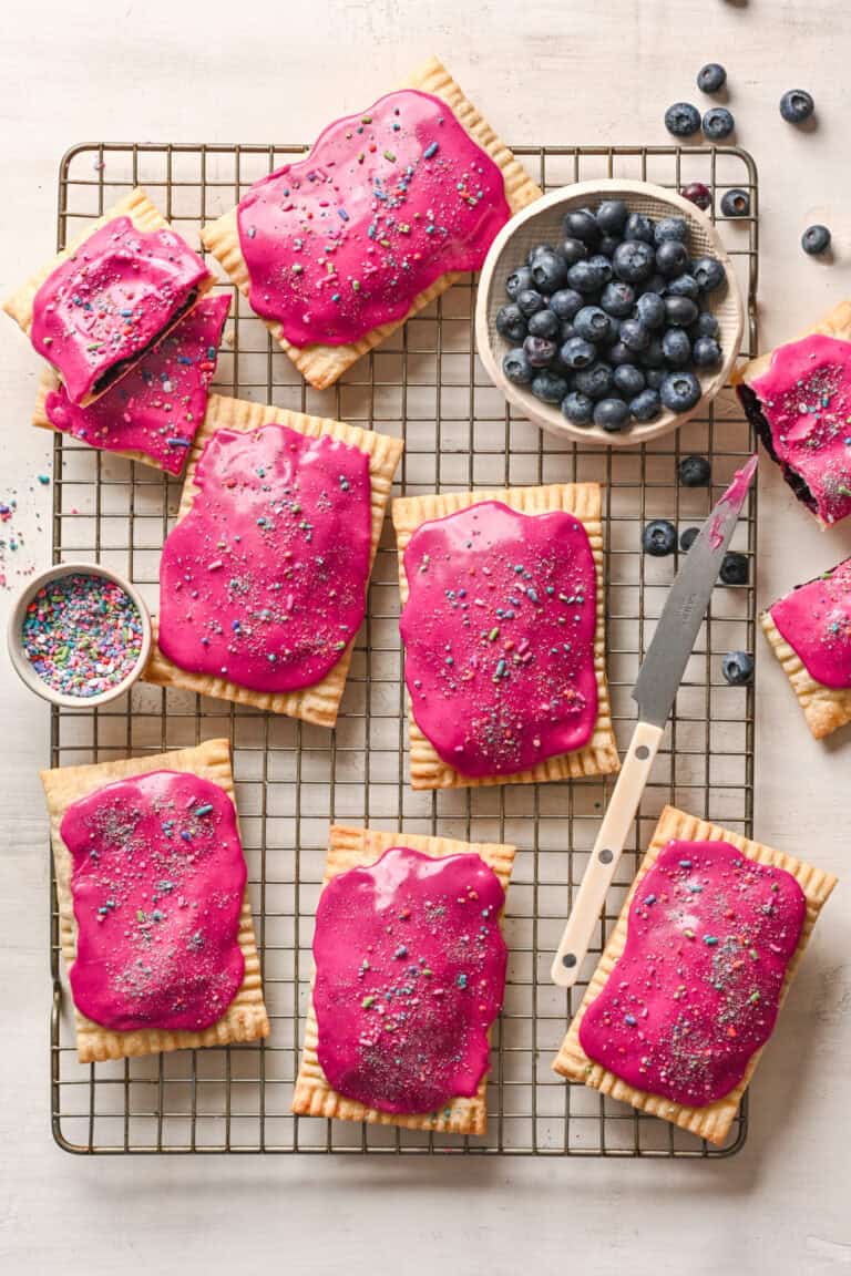overhead view of homemade blueberry pop tarts with bright pink icing and sprinkles on a cooling rack.