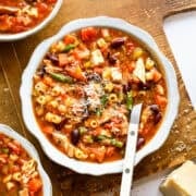 Chicken minestrone soup in a white bowl with a spoon.