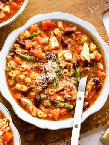 Chicken minestrone soup in a white bowl with a spoon.