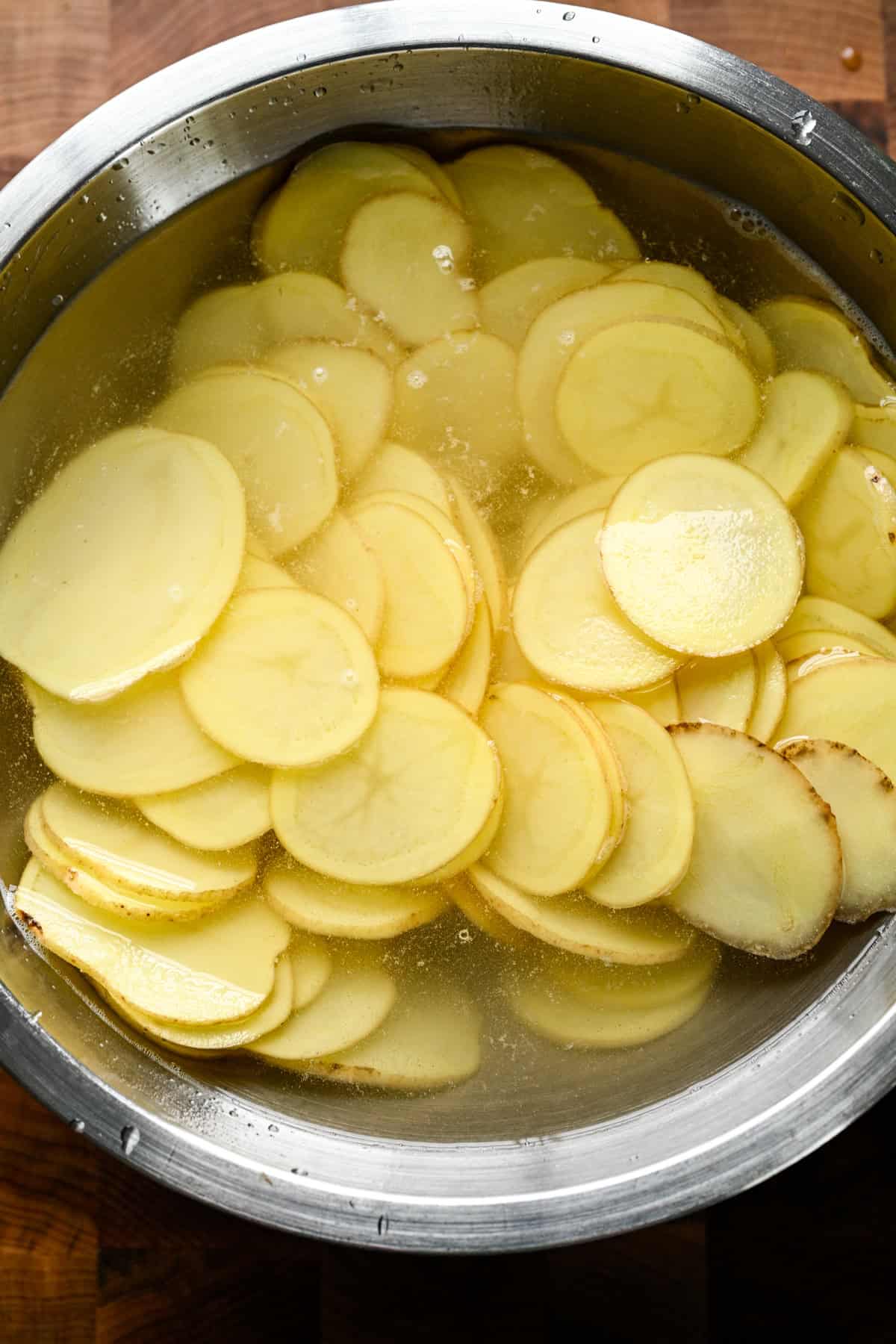 Overhead view of potato slices soaking in cold water.