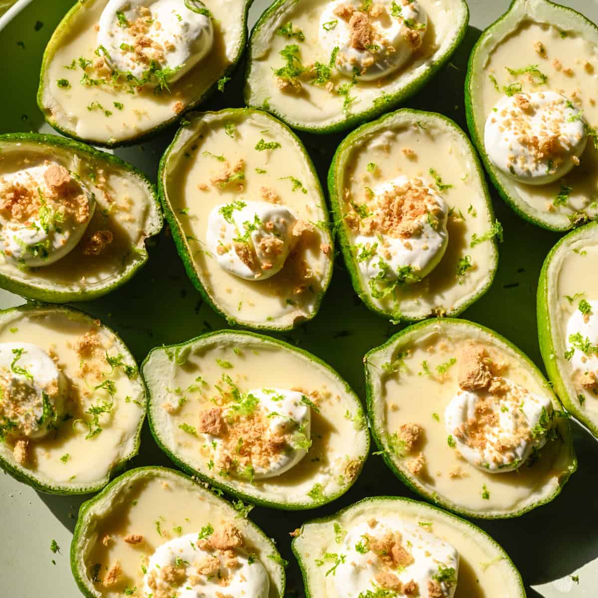 Overhead view of lime possets topped with whipped cream and graham cracker crumbs on light green plate.