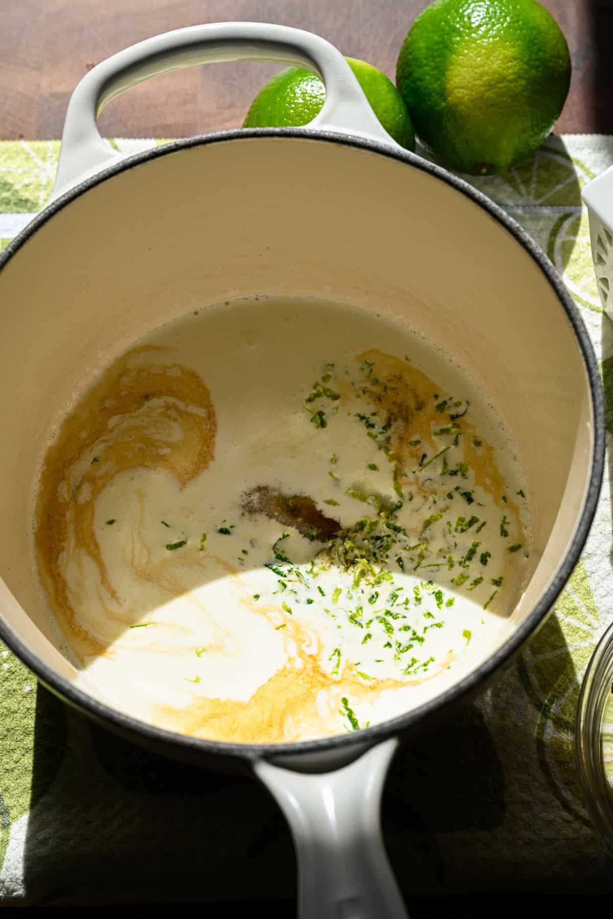 Close up view of heavy cream, lime zest, sugar and vanilla in a white pot.