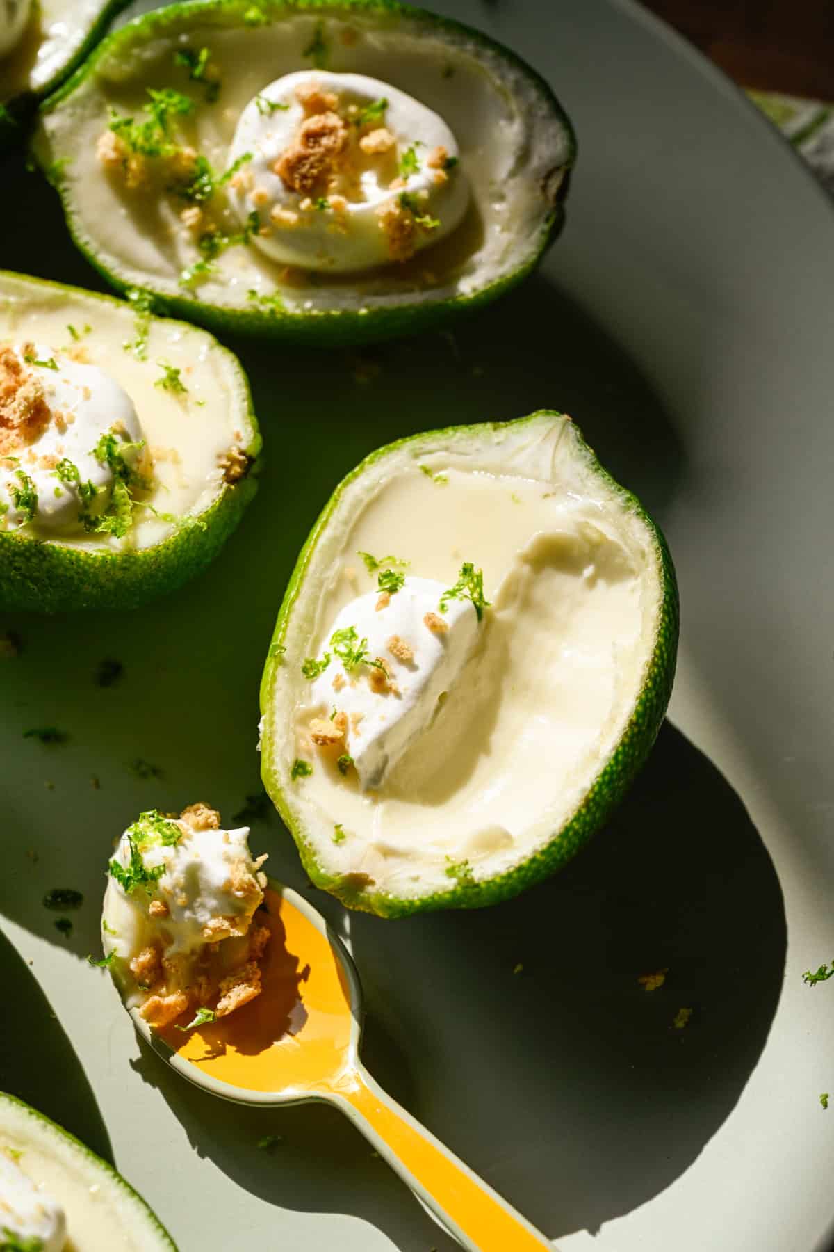 Close up view of lime posset topped with whipped cream and graham cracker crumbs on light green plate with a spoonful taken out.