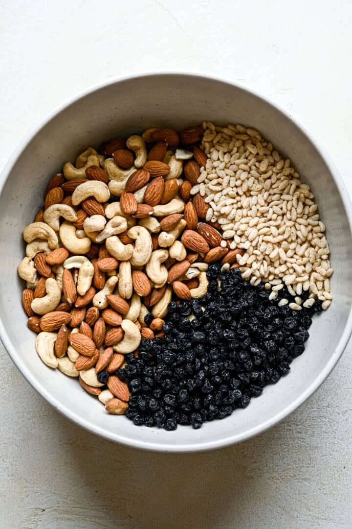 Cashews, almonds, dried blueberries and puffed rice cereal in a bowl before mixing together.