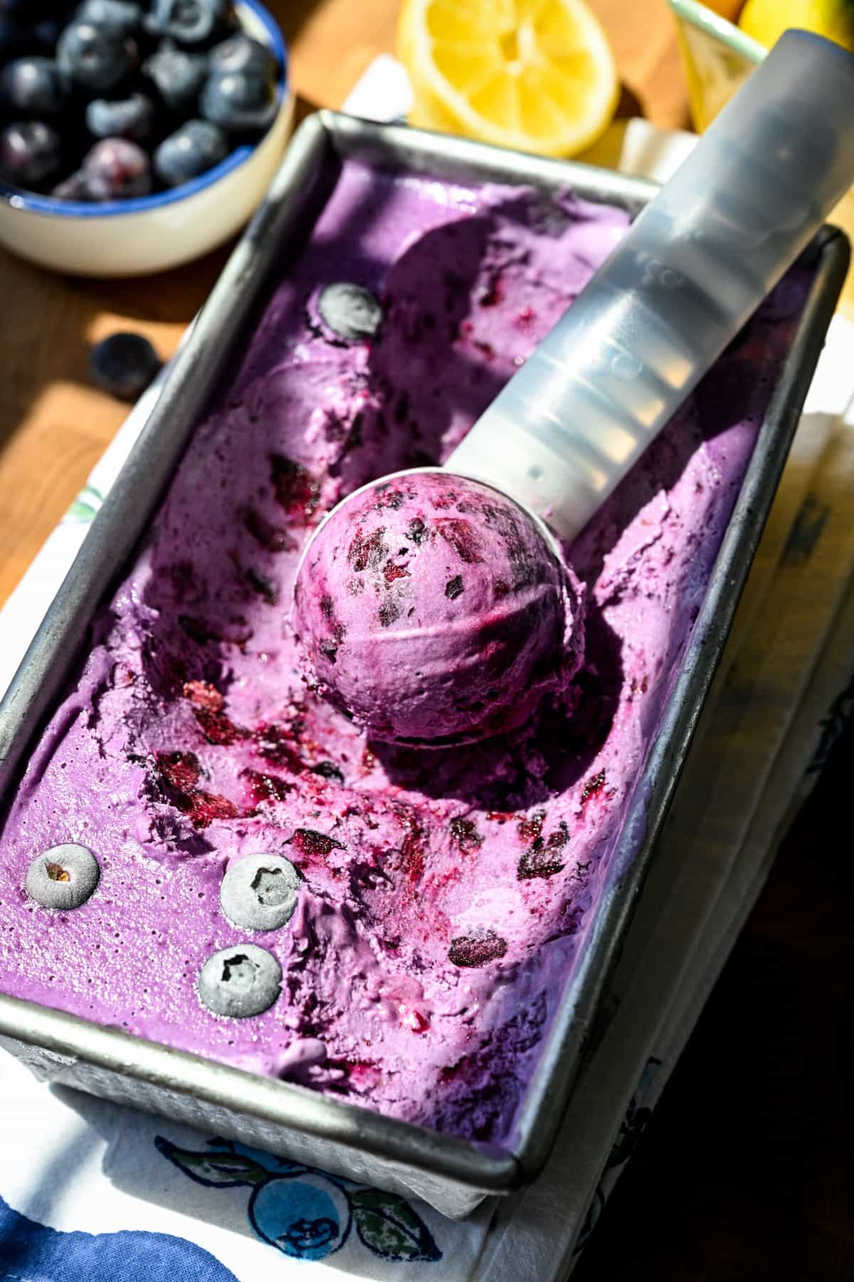 Blueberry lemon ice cream in a loaf pan with an ice cream scoop.