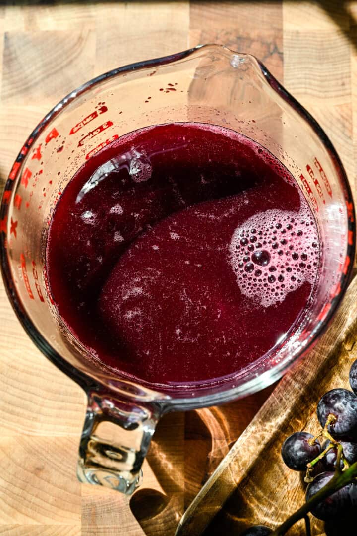 Overhead view of grape soda syrup in a measuring cup.