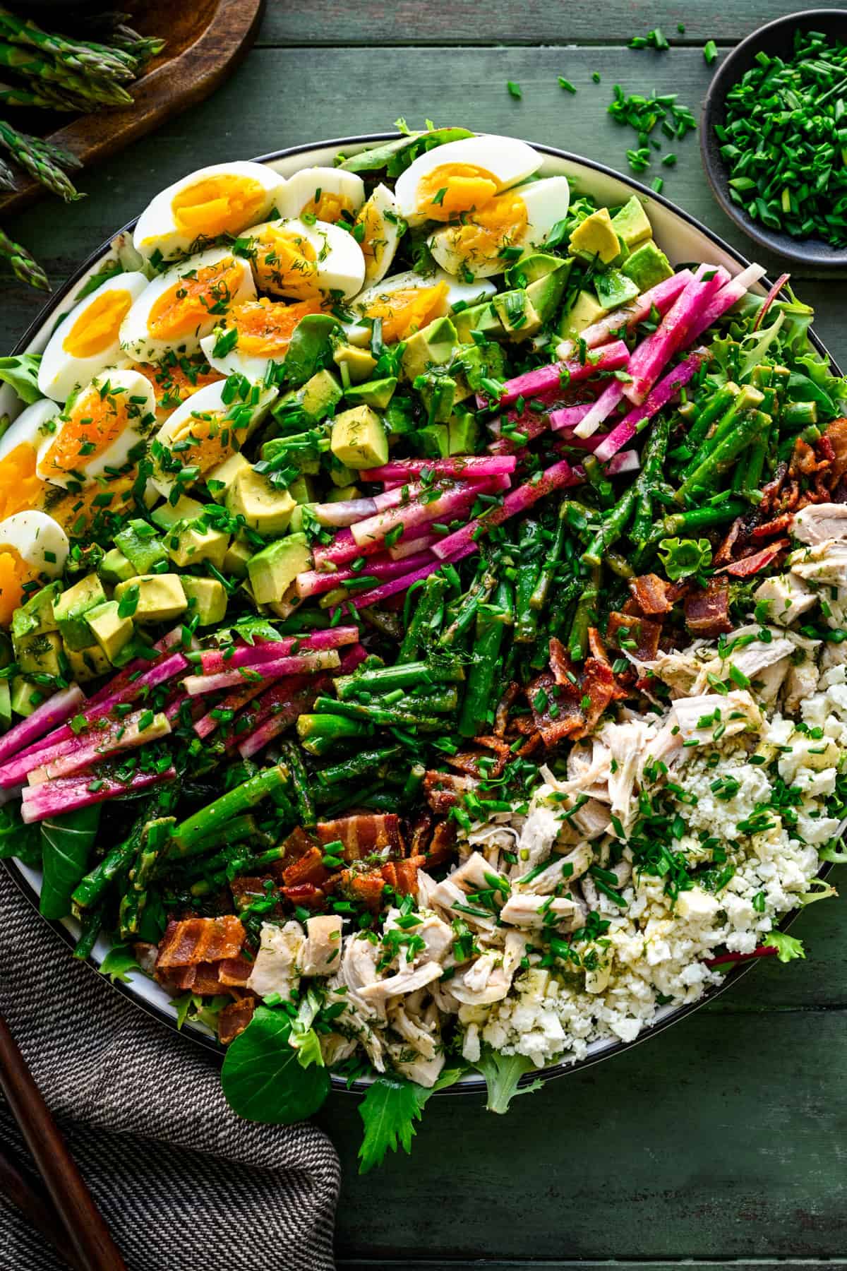 Close up view of spring cobb salad with hard boiled egg, avocado, radish, asparagus, bacon, chicken and feta cheese in rows. 