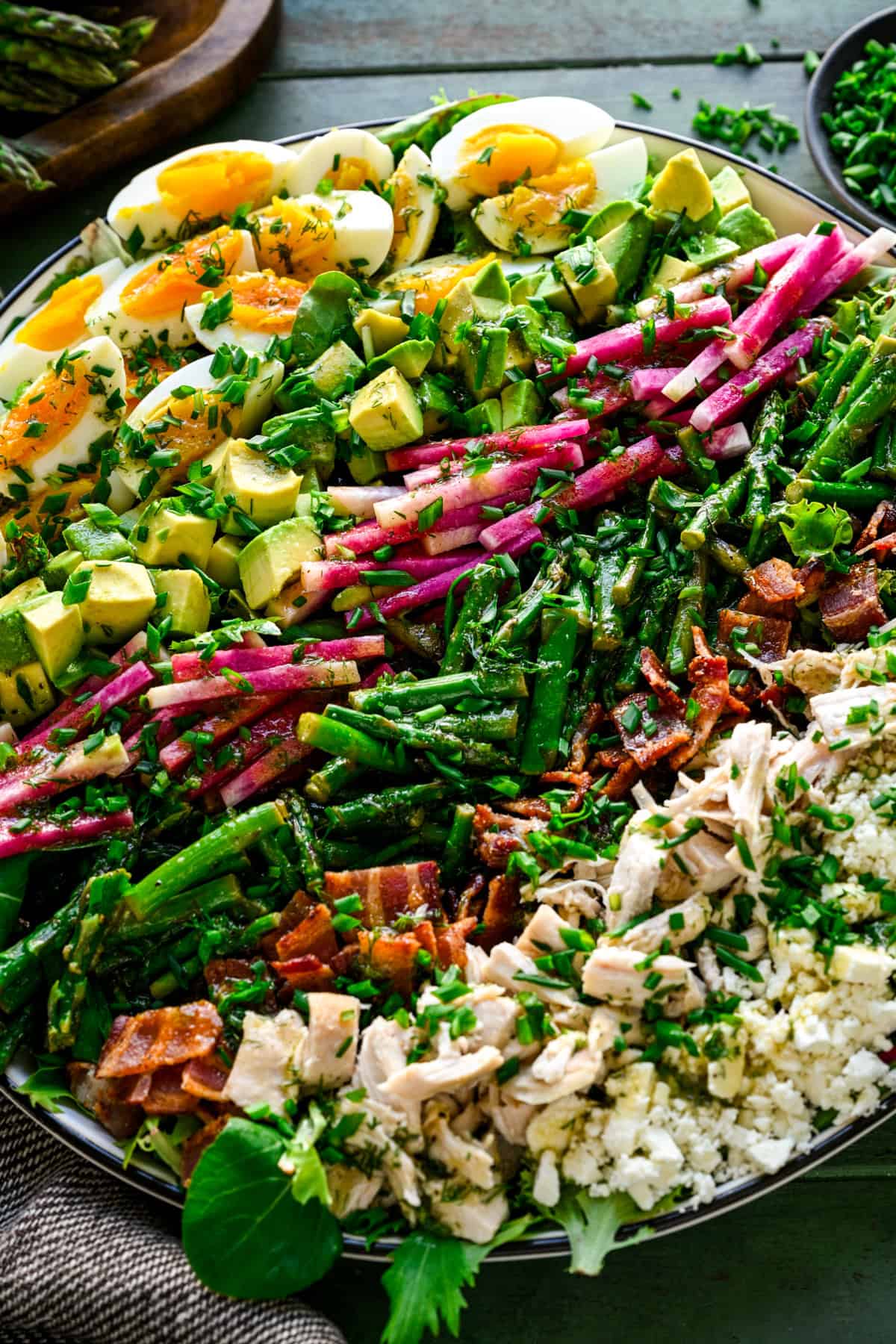 Close up view of spring cobb salad with hard boiled egg, avocado, radish, asparagus, bacon, chicken and feta cheese in rows.