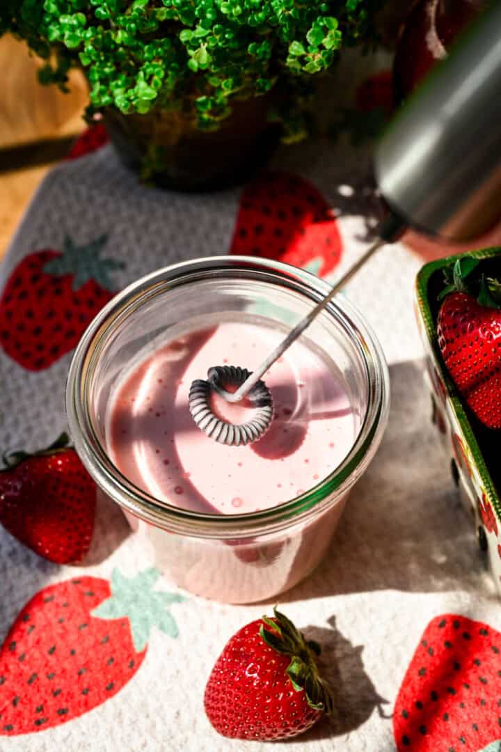 Strawberry cold foam in a jar with hand mixer.