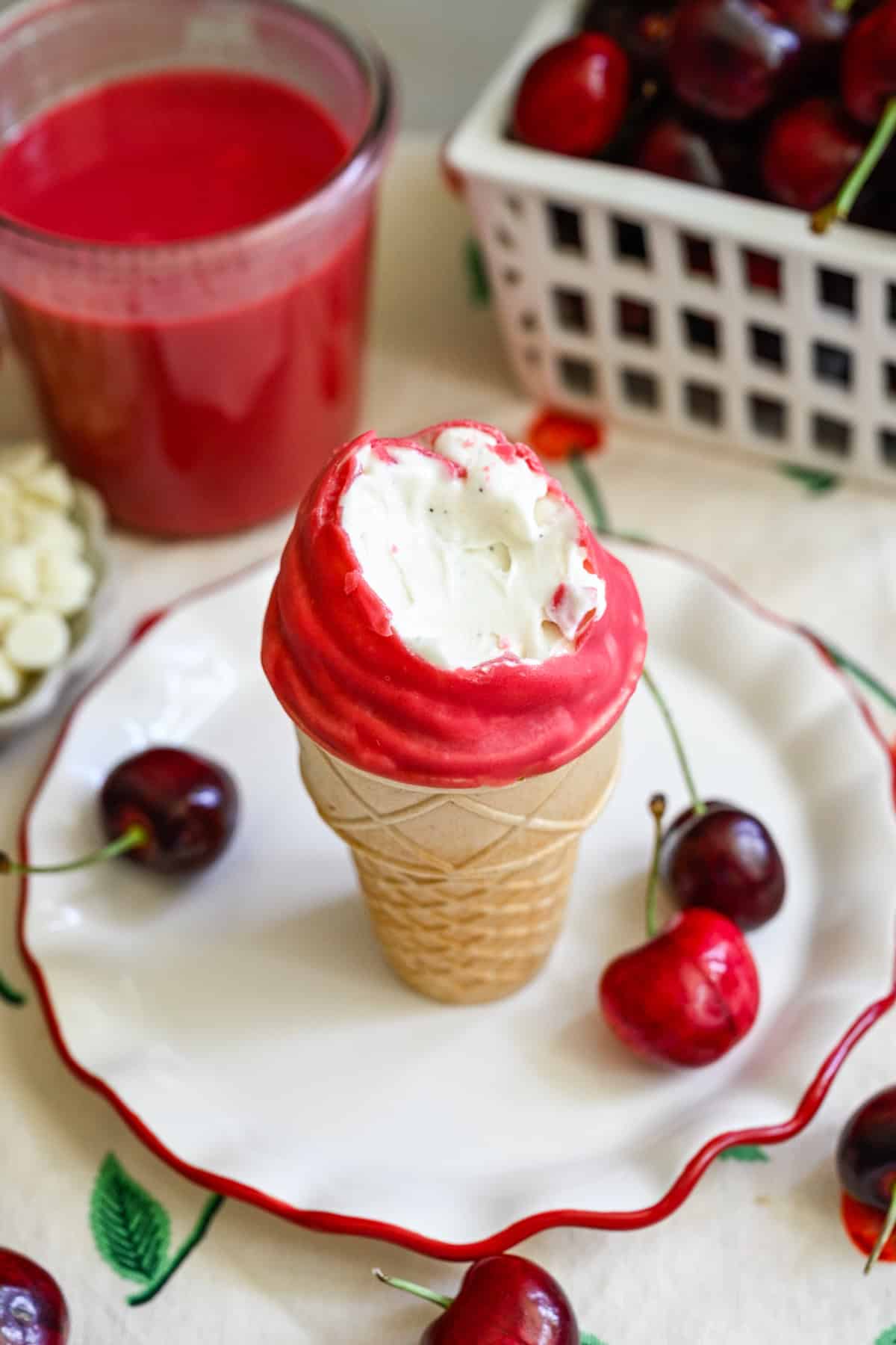 Ice cream cone with vanilla swirl dipped in homemade cherry magic shell with a bite taken out to show the ice cream.