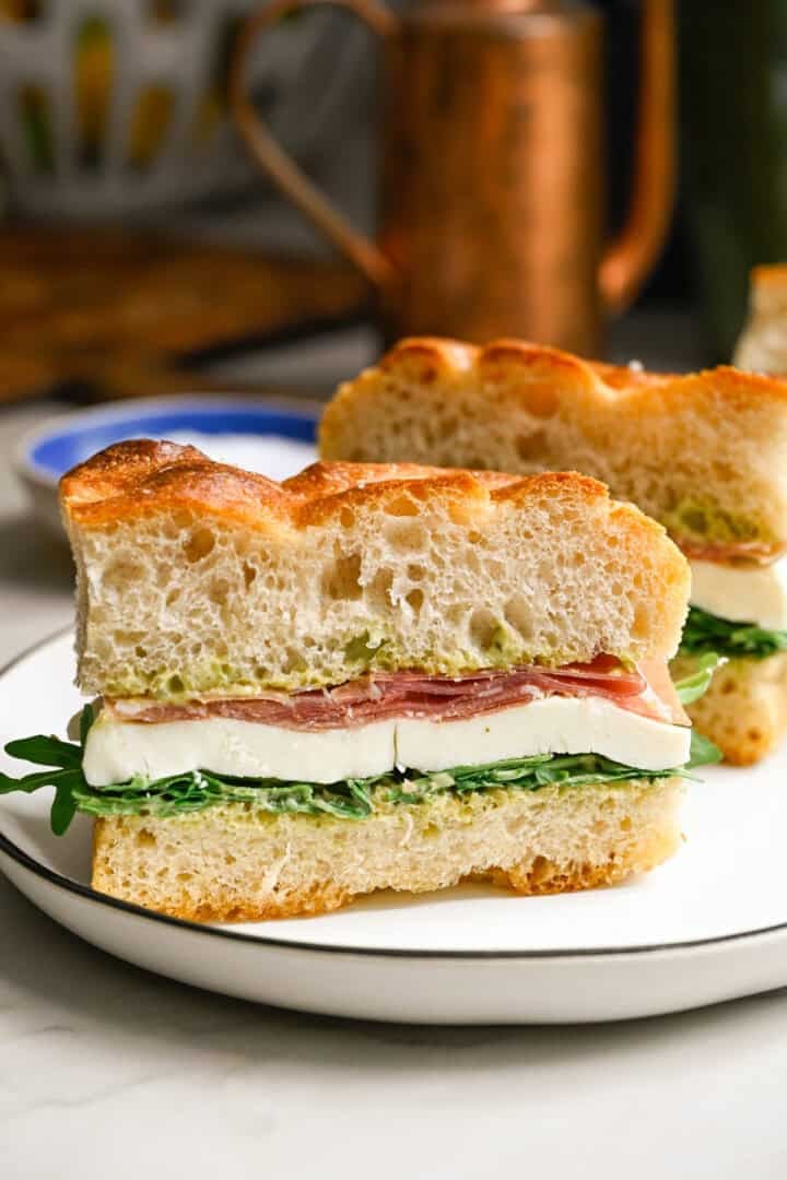Close up side view of a focaccia sandwich with pesto aioli, arugula, fresh mozzarella and prosciutto.