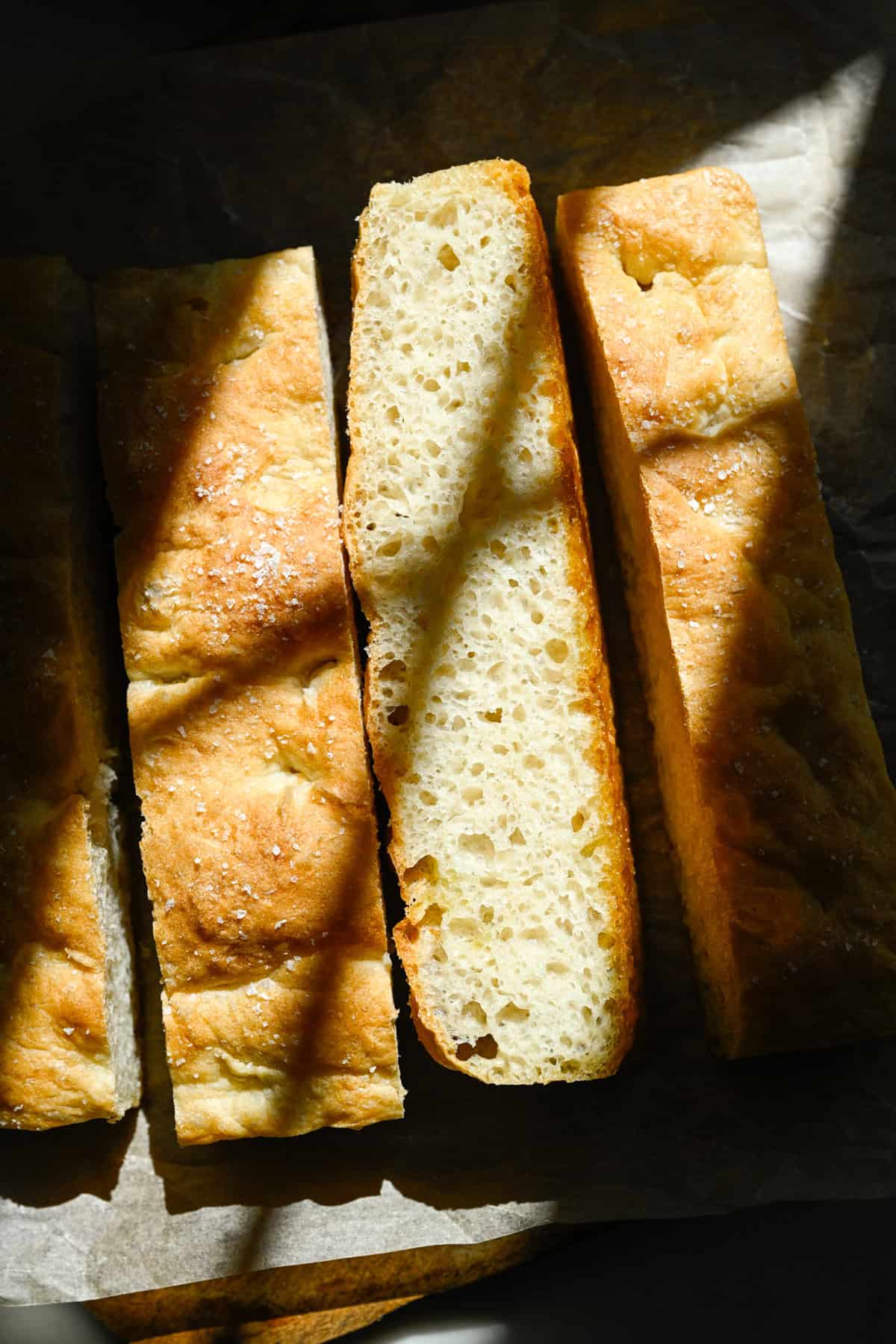 Overhead of homemade focaccia bread sliced into 4 long pieces.