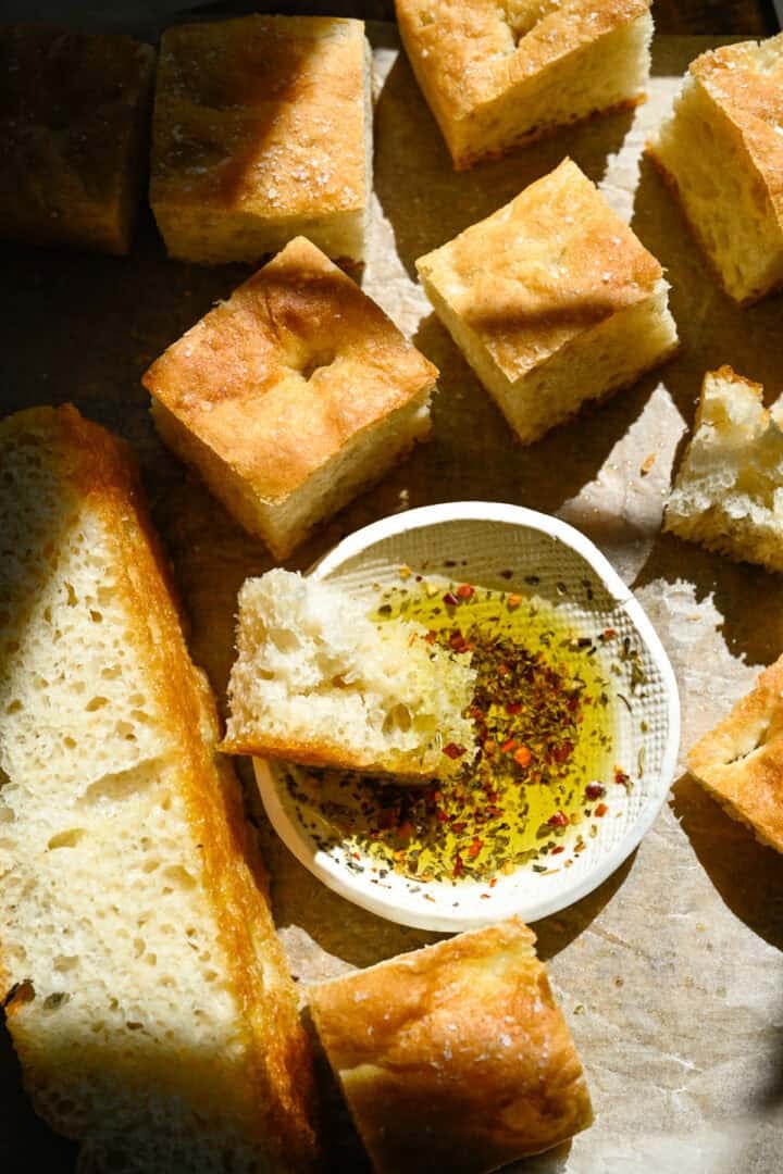 Overhead view of focaccia slices with some dipped in seasoned olive oil in a small white bowl.