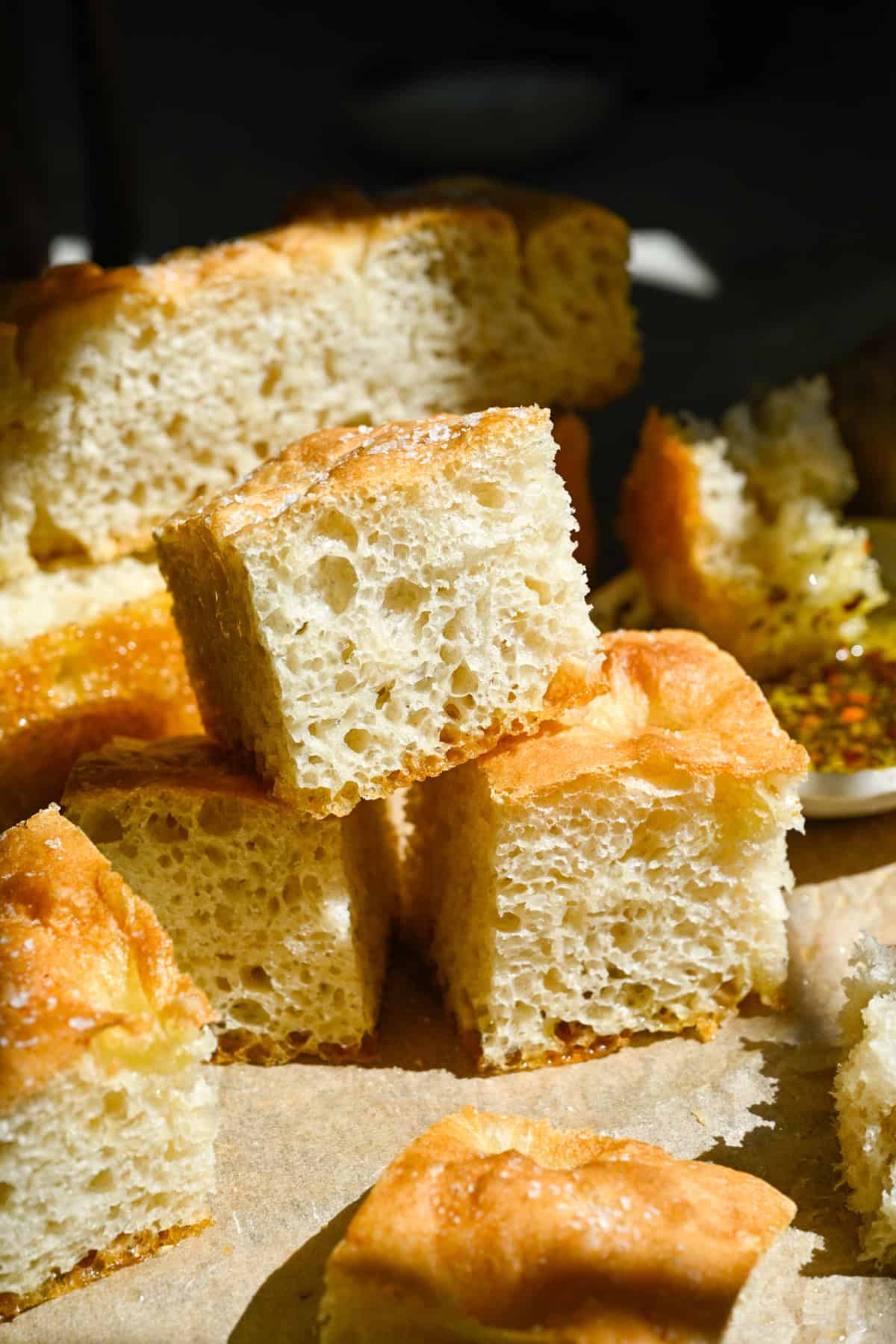 Close up view of 3 pieces of homemade focaccia stacked on parchment paper. 