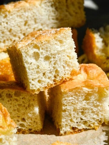Close up view of 3 pieces of homemade focaccia stacked on parchment paper.