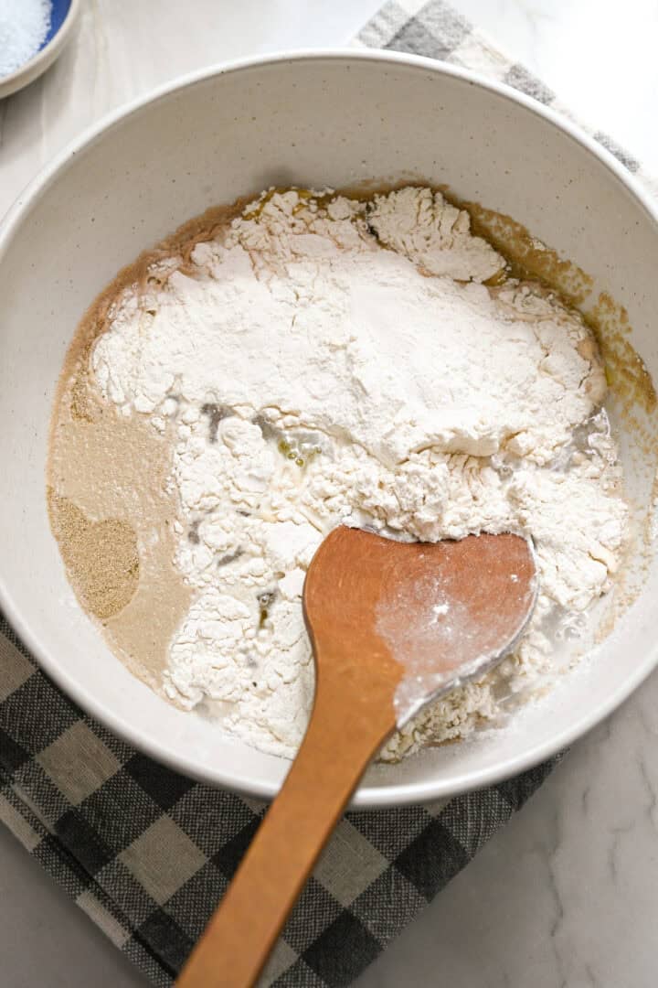 Water, yeast, olive oil and flour in a mixing bowl before mixing together.