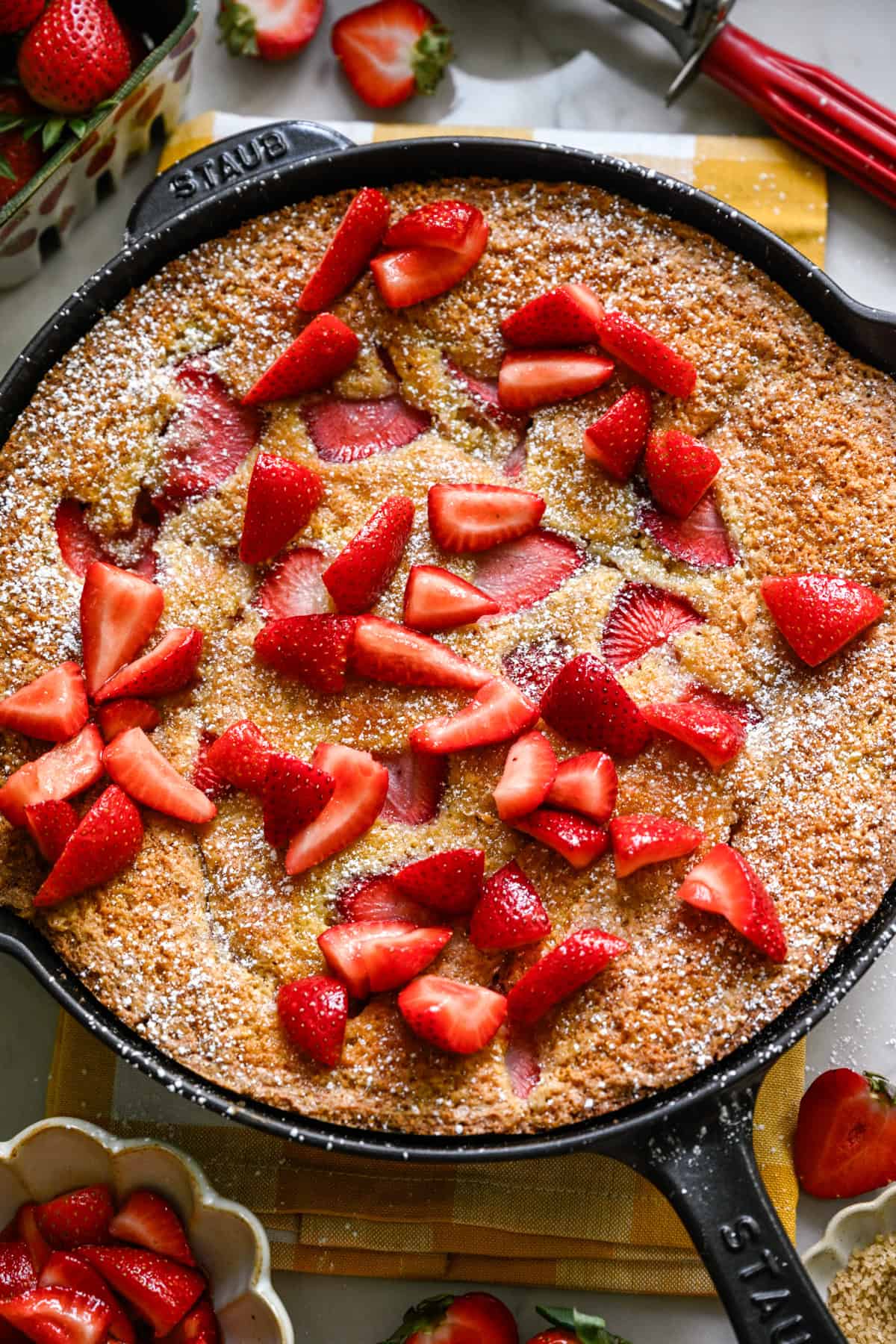 Overhead view of strawberry cornmeal cake in a cast iron skillet topped with more strawberries.