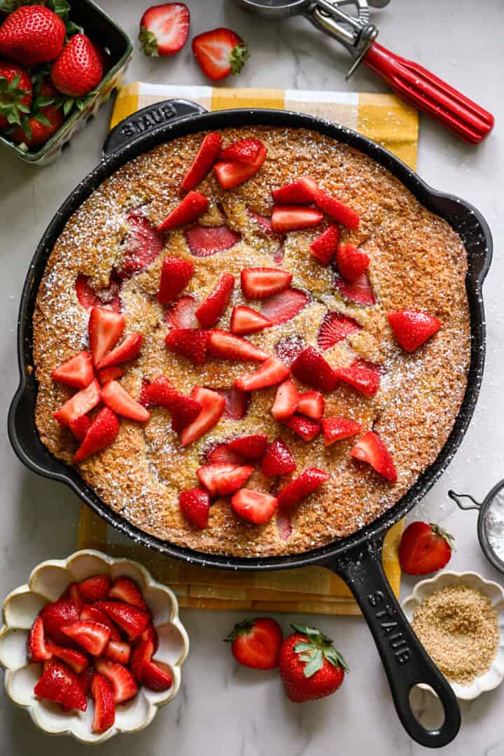 Overhead view of strawberry cornmeal cake in a cast iron skillet topped with more strawberries.