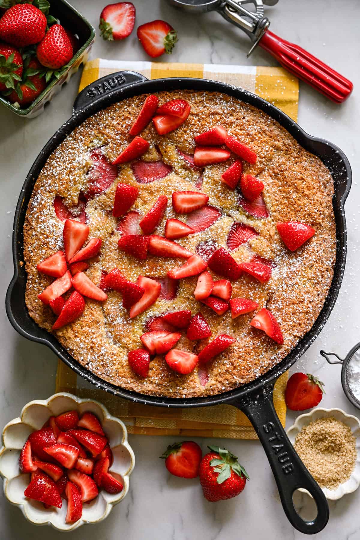 Overhead view of strawberry cornmeal cake in a cast iron skillet topped with more strawberries.