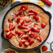 Overhead view of strawberry cornmeal cake in a cast iron skillet topped with more strawberries.