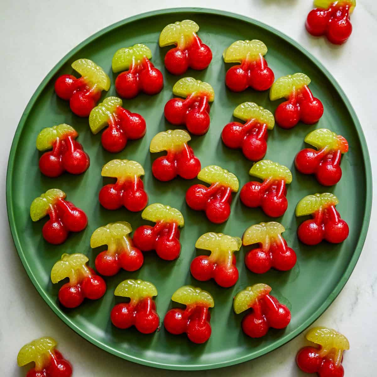 Overhead view of several cherry gummies on a green plate.