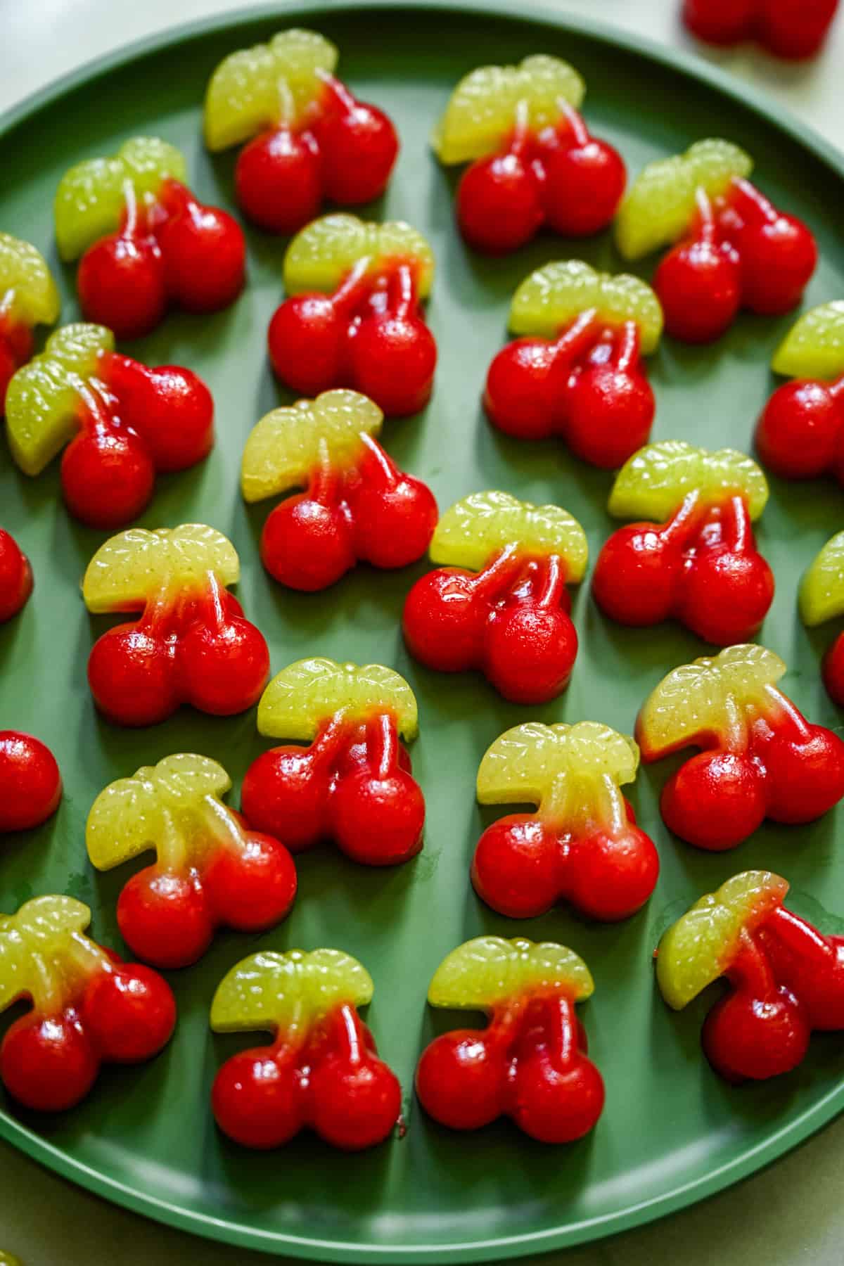 Overhead view of several cherry gummies on a green plate.