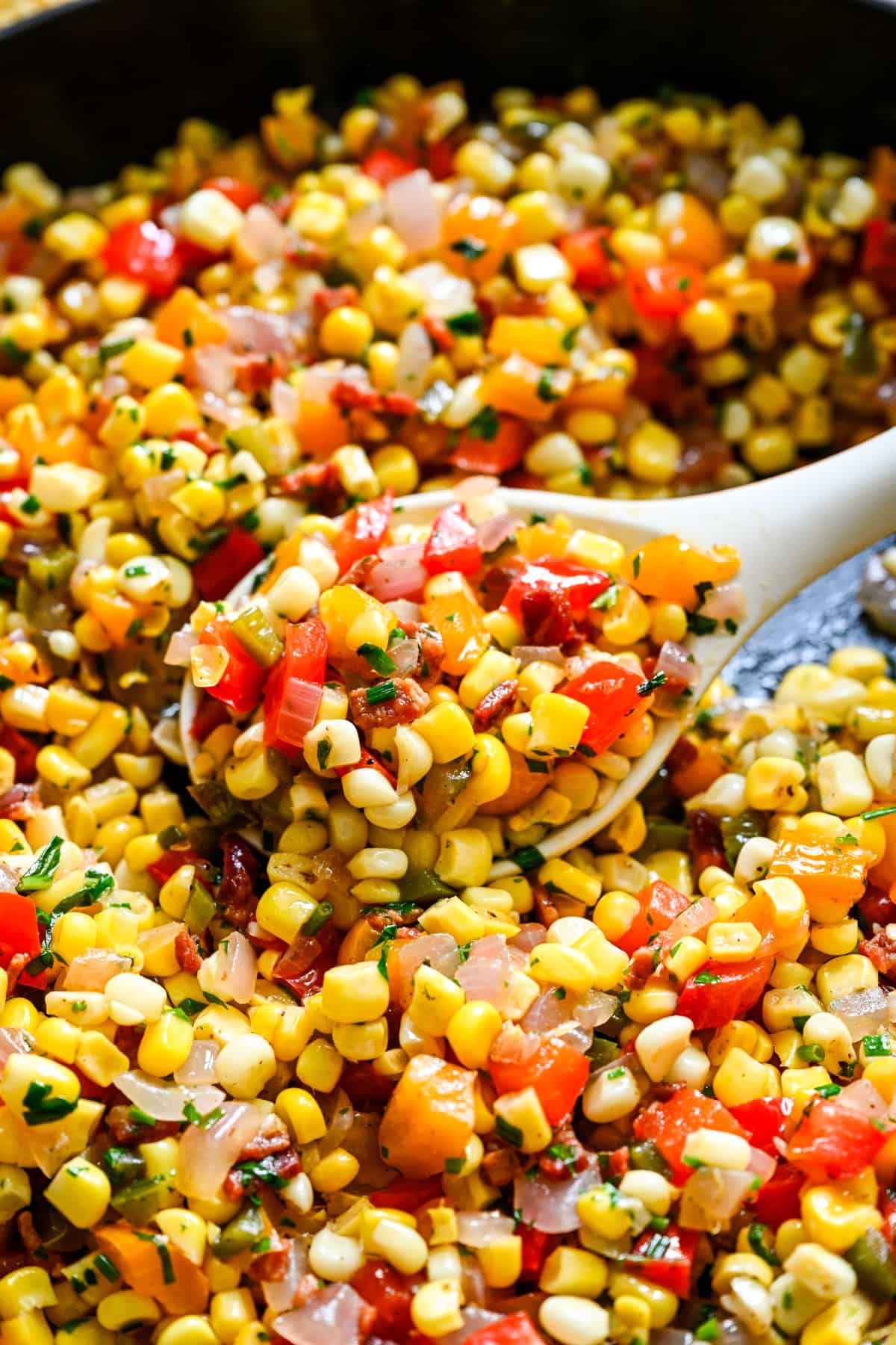 Close up view of confetti corn on a serving spoon in a skillet.