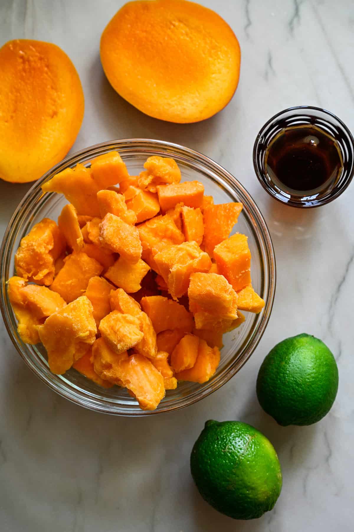 overhead view of diced mango in a bowl, 2 limes, and agave syrup on the countertop.