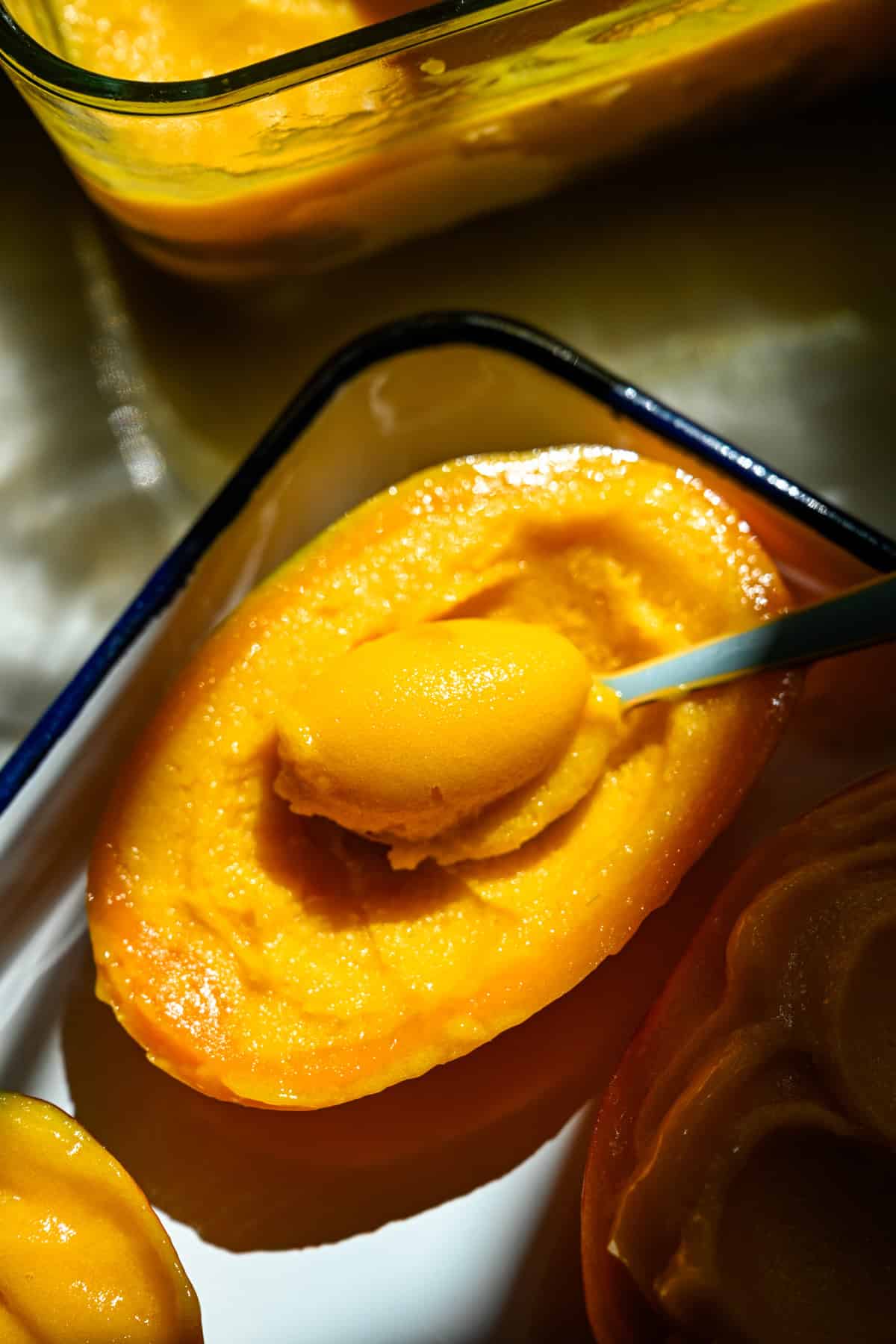 Mango sorbet in a mango half with a spoon in it.