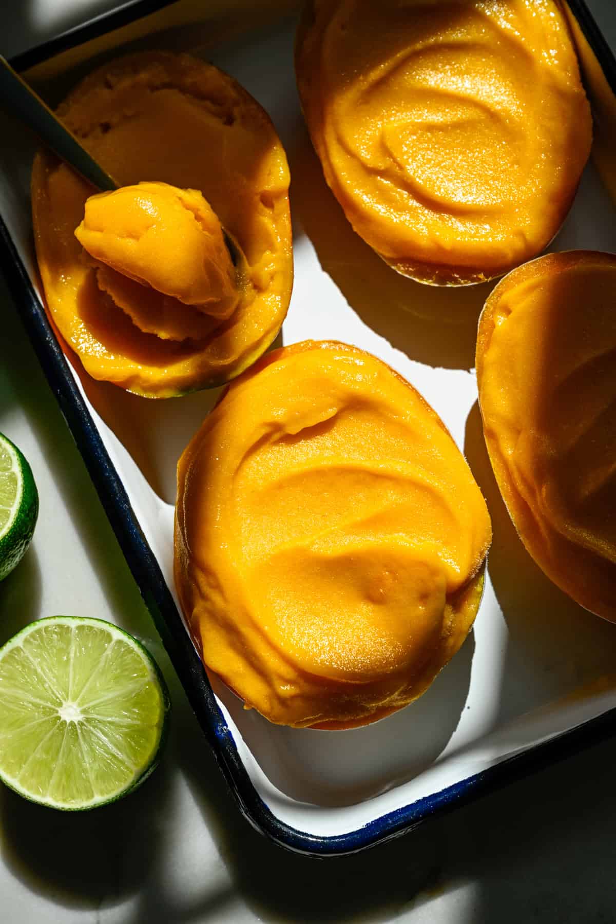 Overhead view of mango sorbet in a mango half on a sheet pan with a few others.