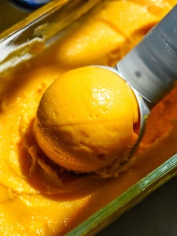 Close up view of a scoop of mango sorbet sitting in a container of sorbet.