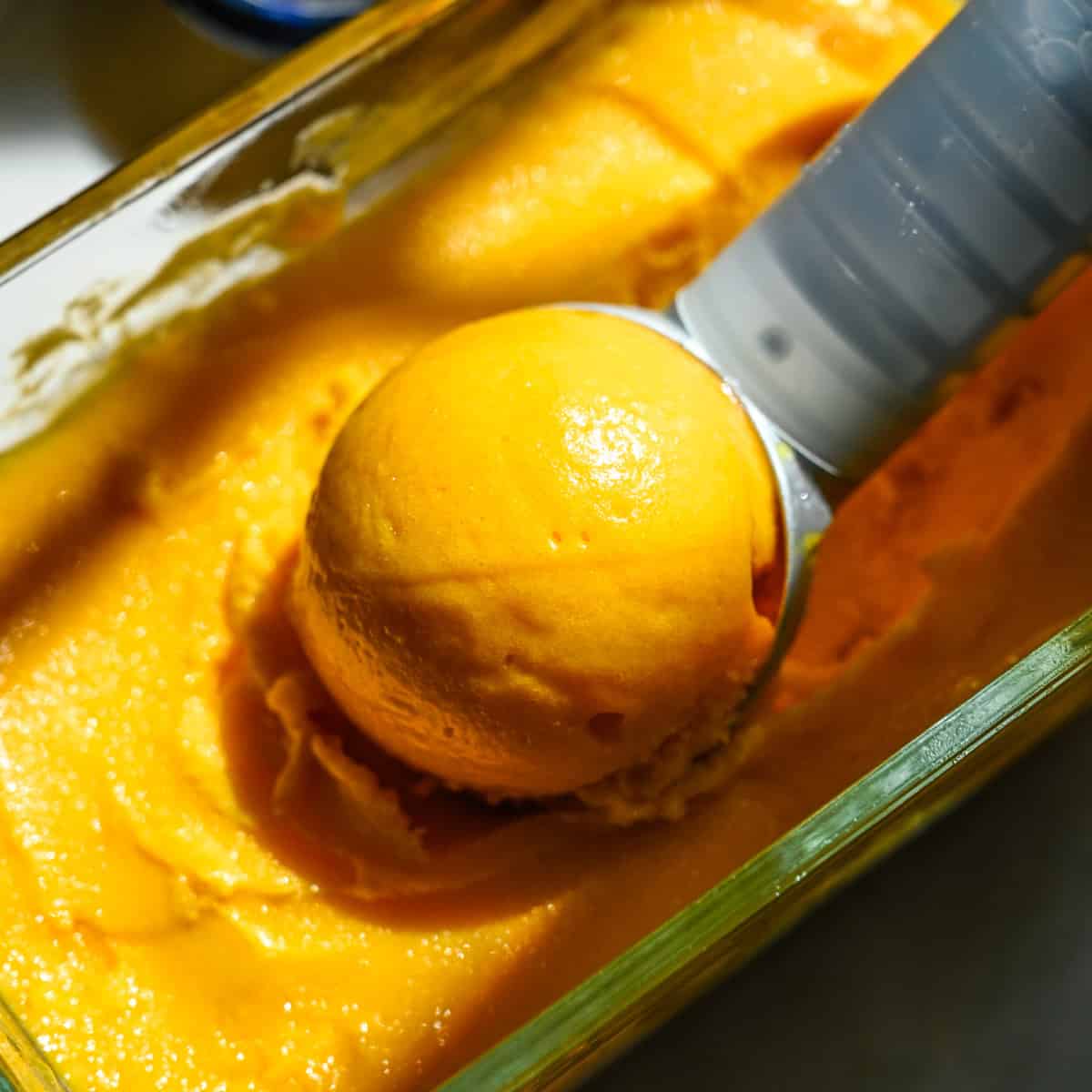 Close up view of a scoop of mango sorbet sitting in a container of sorbet.