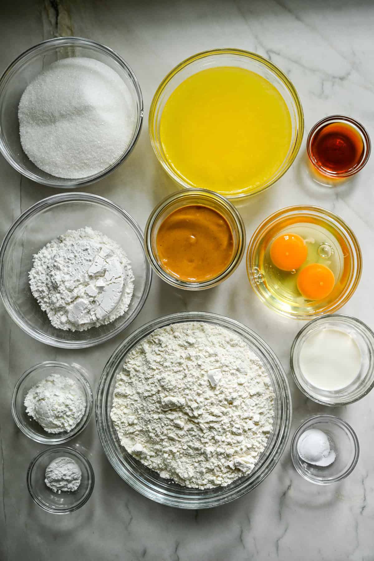 Overhead view of ingredients for homemade nutter butters in separate prep bowls on white countertop.