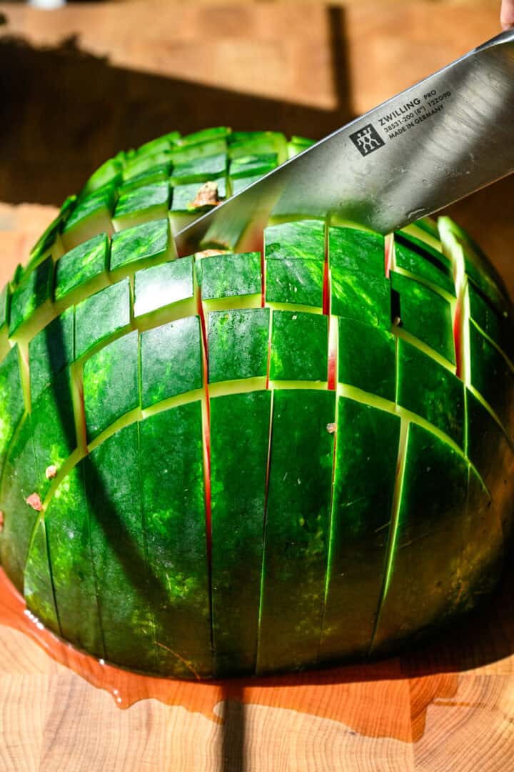 Cutting half of a watermelon into 1 inch square sticks.