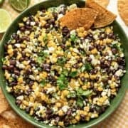 Overhead view of black bean corn feta dip in a green bowl with tortilla chips on the side.