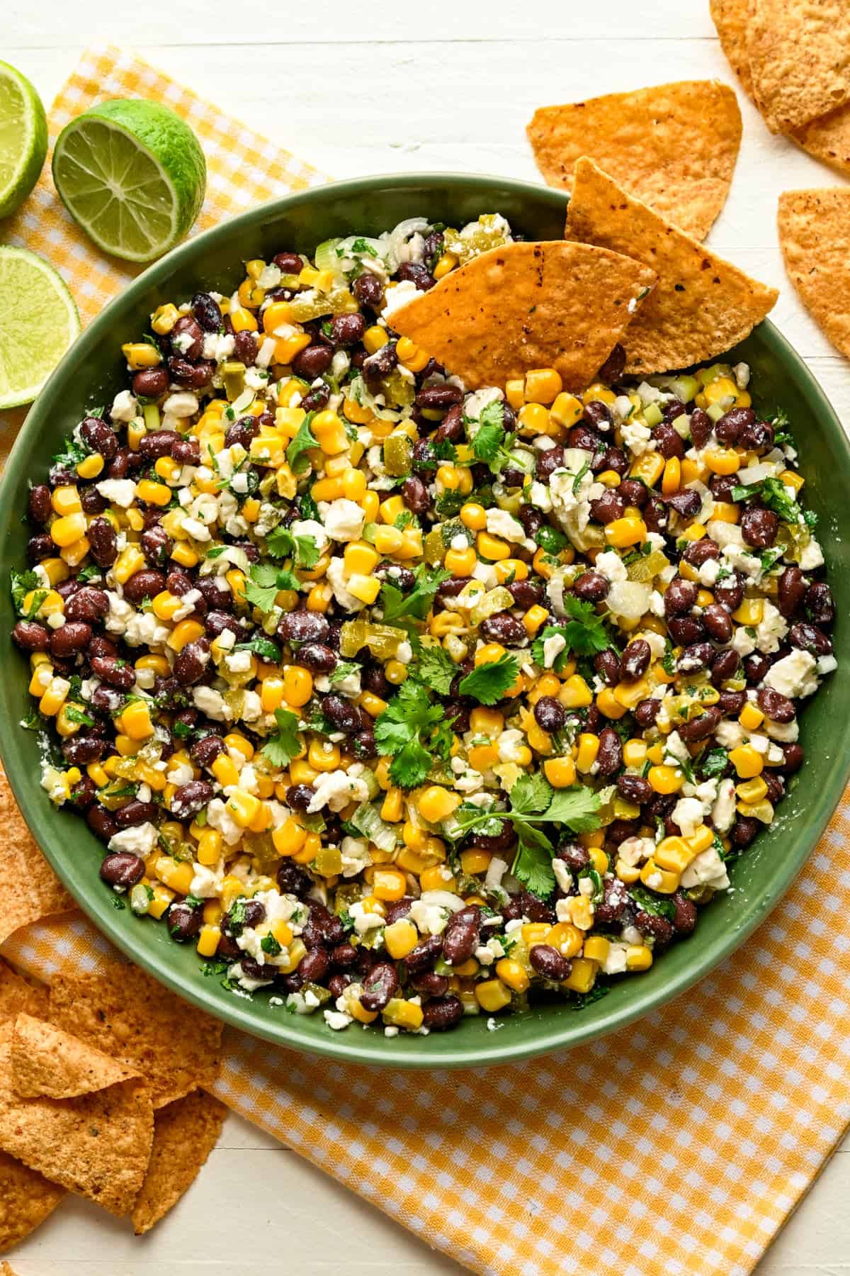 Overhead view of black bean corn feta dip in a green bowl with tortilla chips on the side. 
