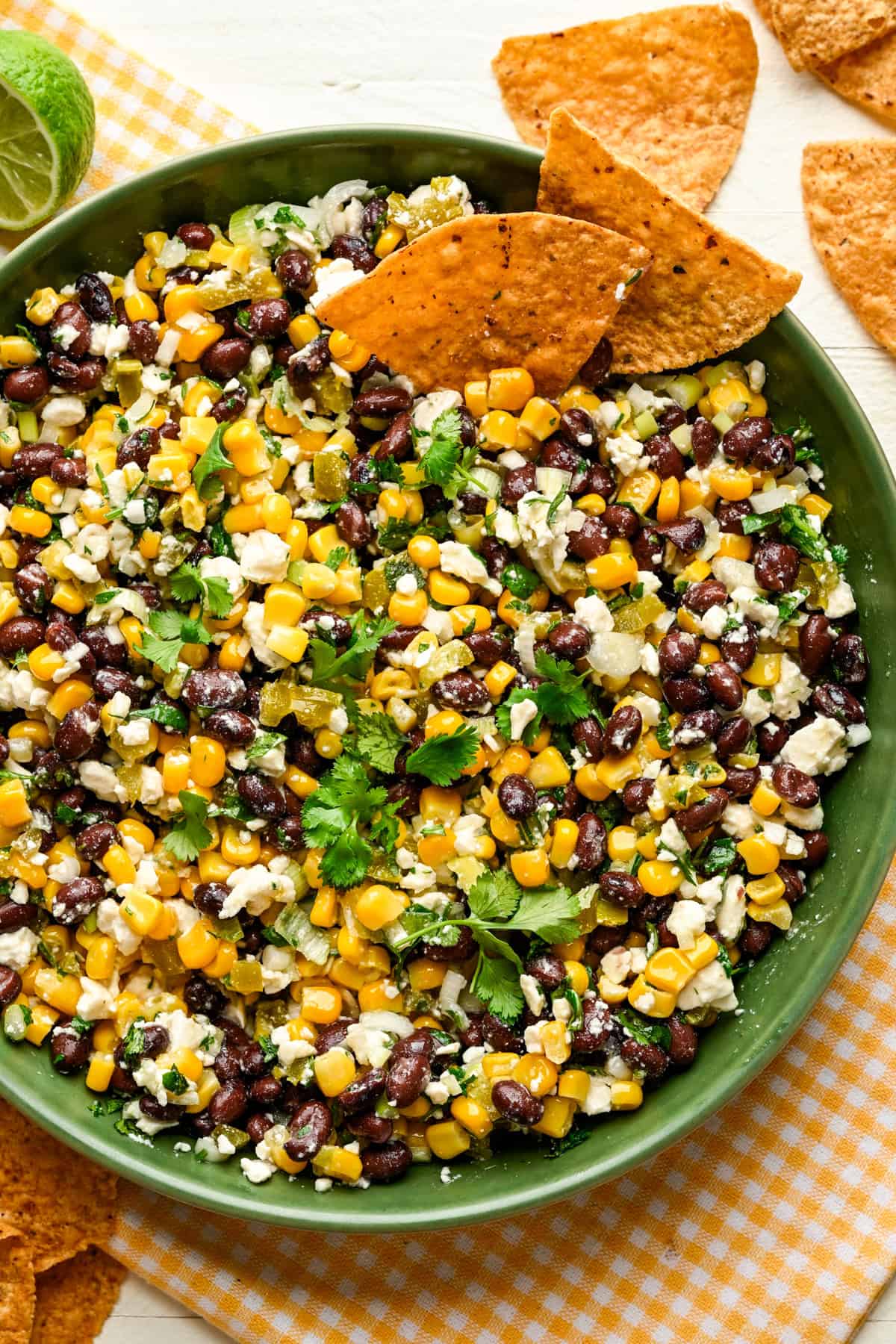 Overhead view of black bean corn feta dip in a green bowl with tortilla chips on the side.
