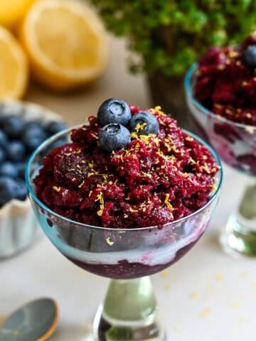 Blueberry granita in a cocktail glass topped with blueberries and lemon zest.
